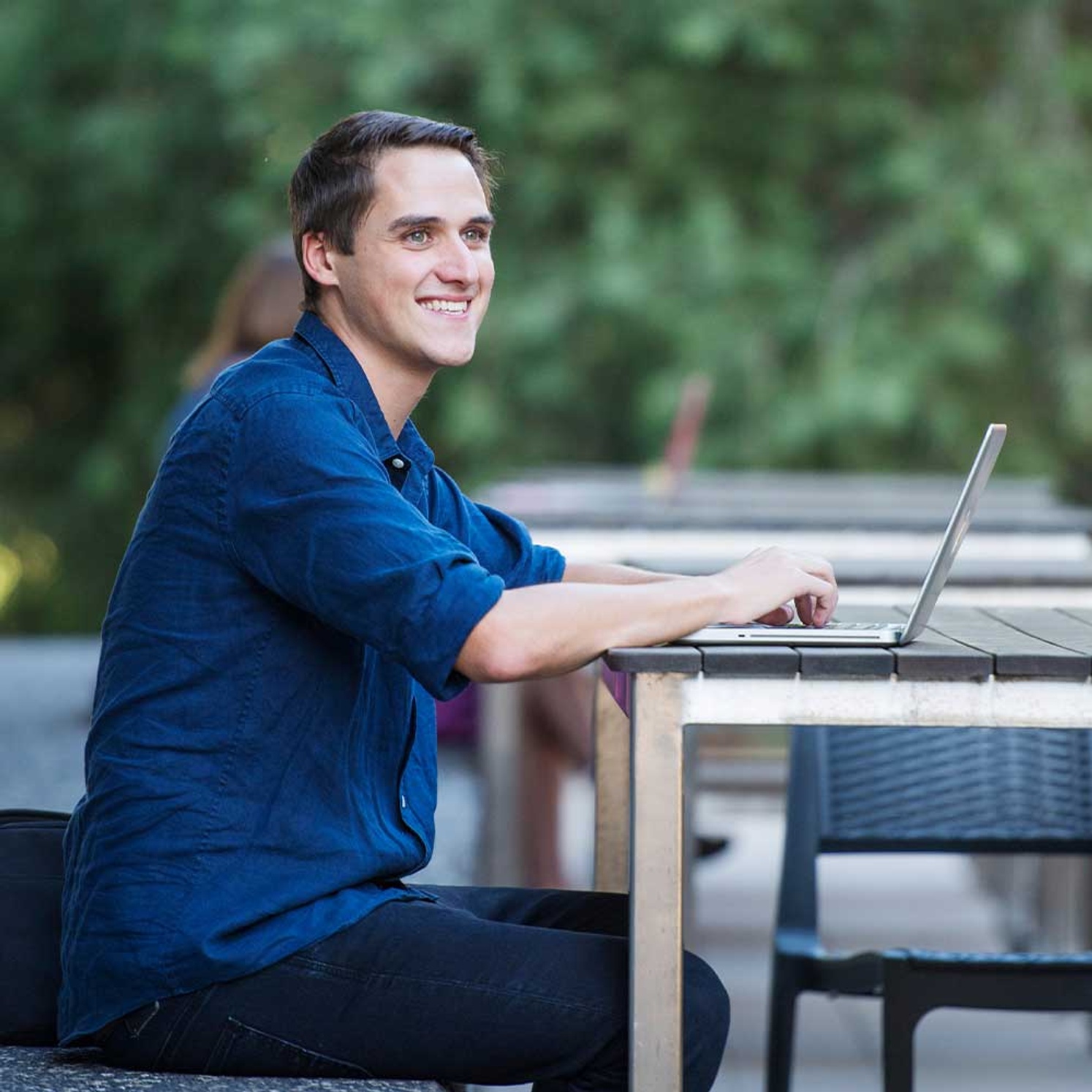 Male student sitting outside with a laptop