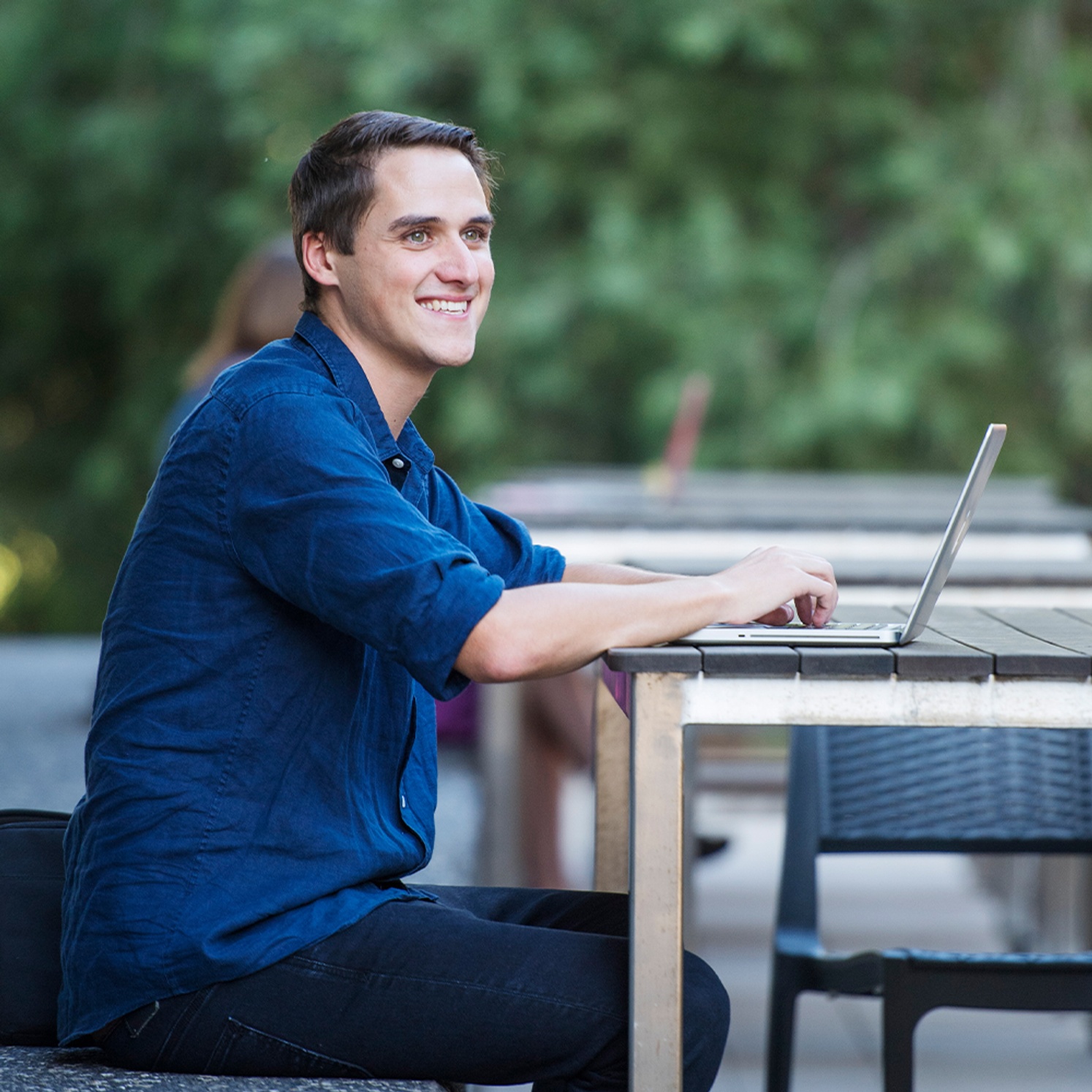 Male student sitting outside with a laptop