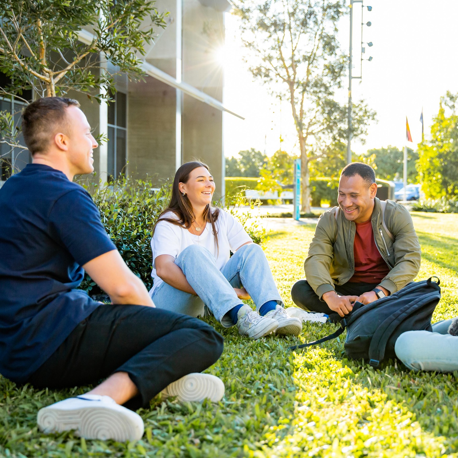 Three students sitting on the grass smiling and talking