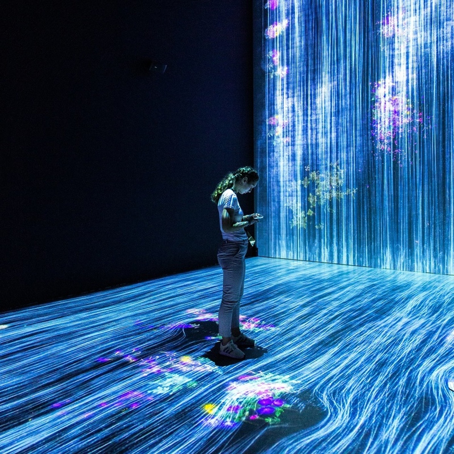 A girl stands in an immersive art installation looking at her phone