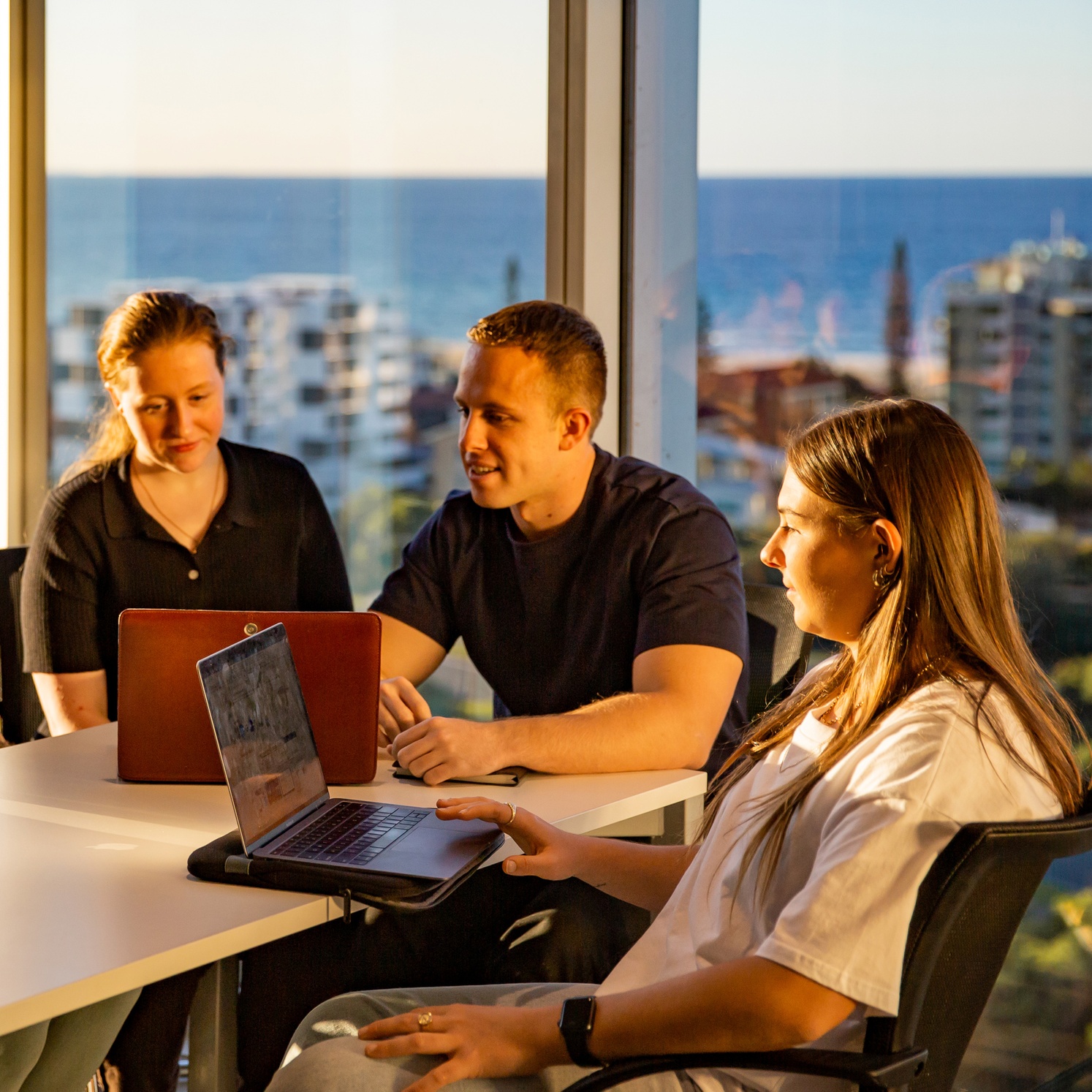 Three students working at the Gold Coast campus with ocean views in the background