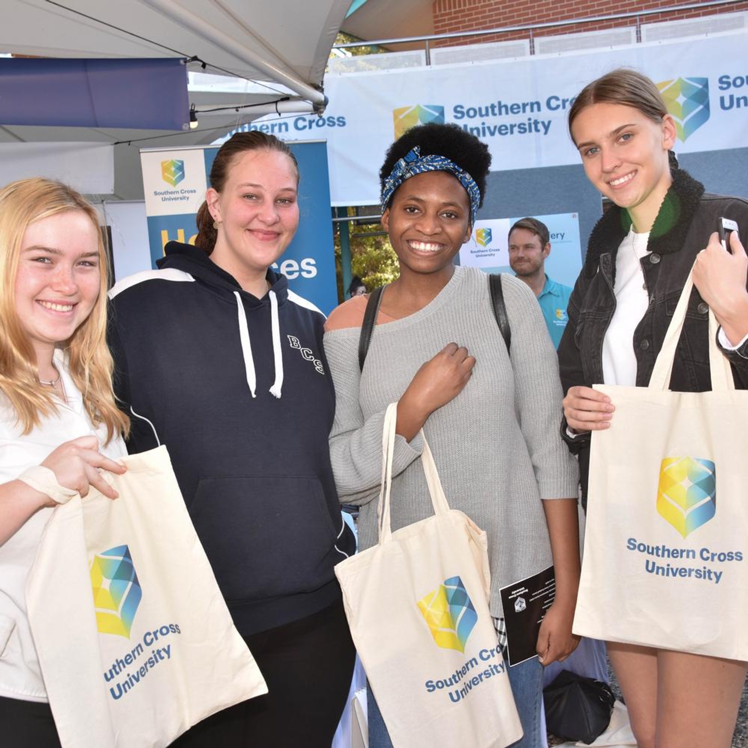 Four students holding Southern Cross tote bags at open day.