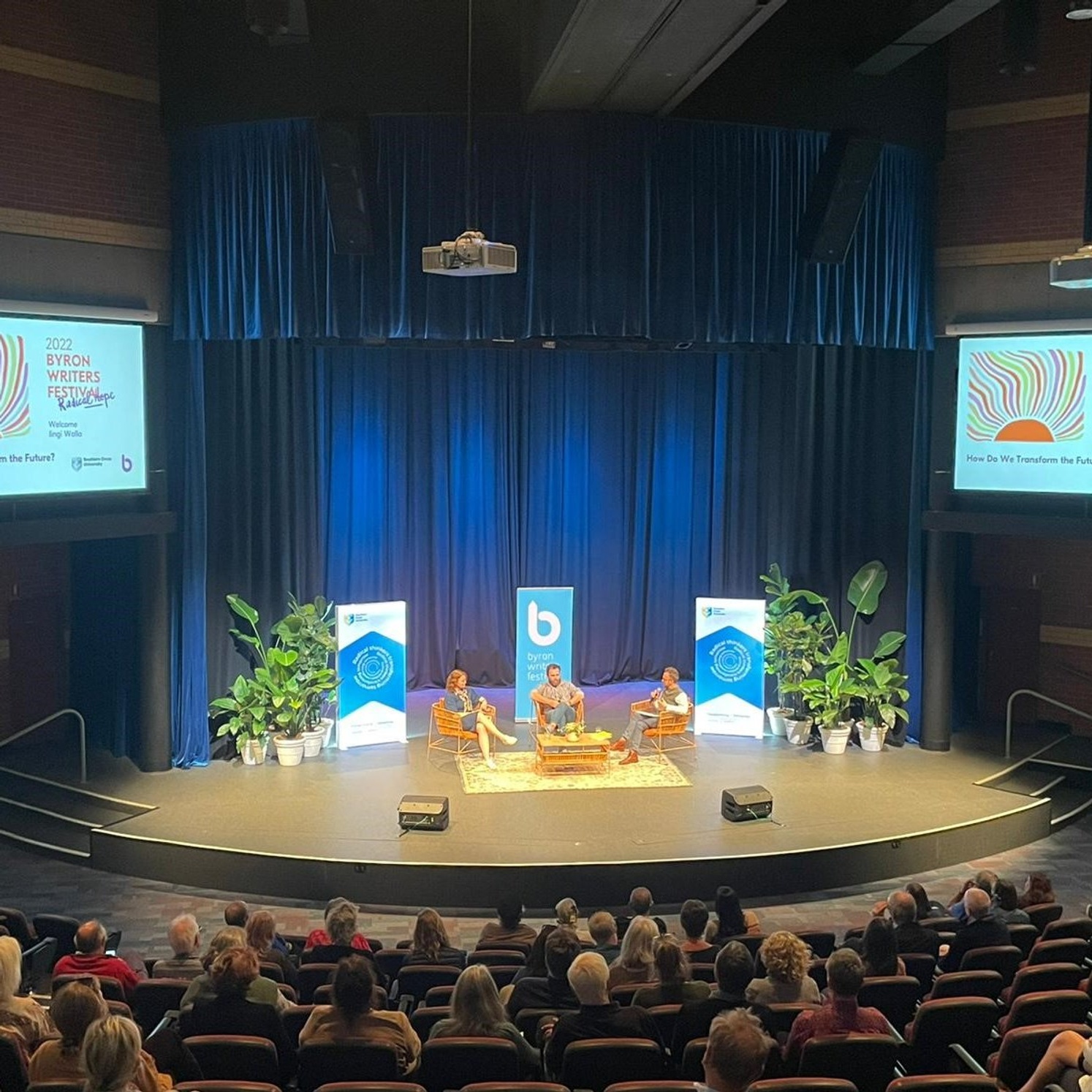 Crowd surround stage where three panelist discuss at Byron Writers Festival