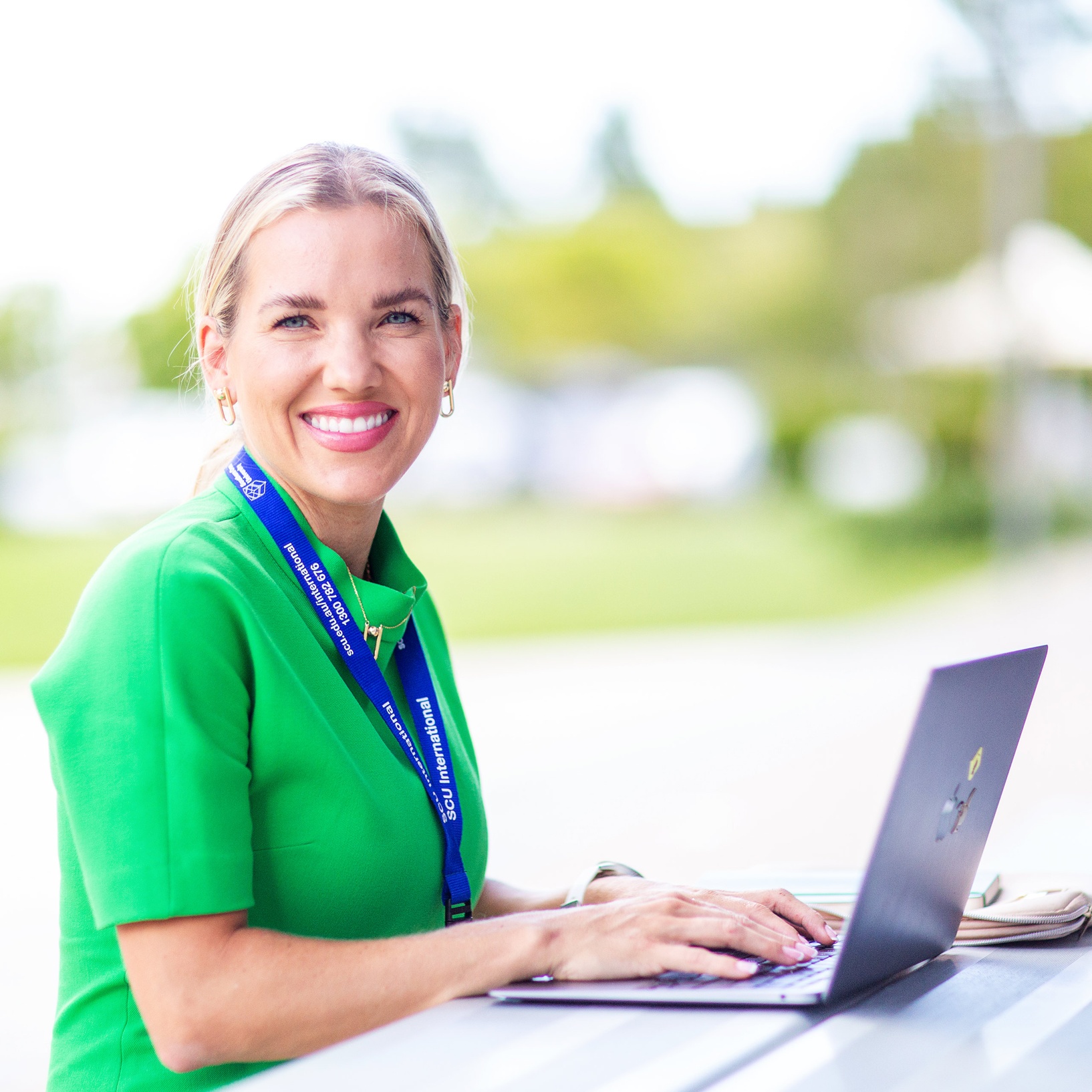 student smiling in the outdoors on computer