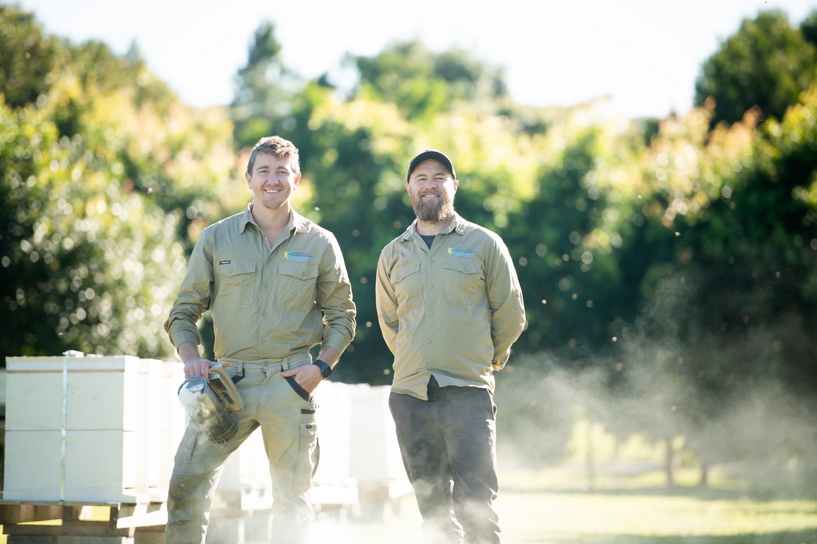 Two men in a field with bee hives in the background
