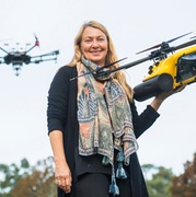 Dr Debra Stokes holding a drone with another drone flying in background