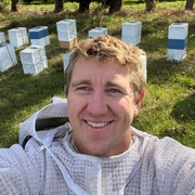 Head and shoulders of Cooper Schouten with Bee hives in background
