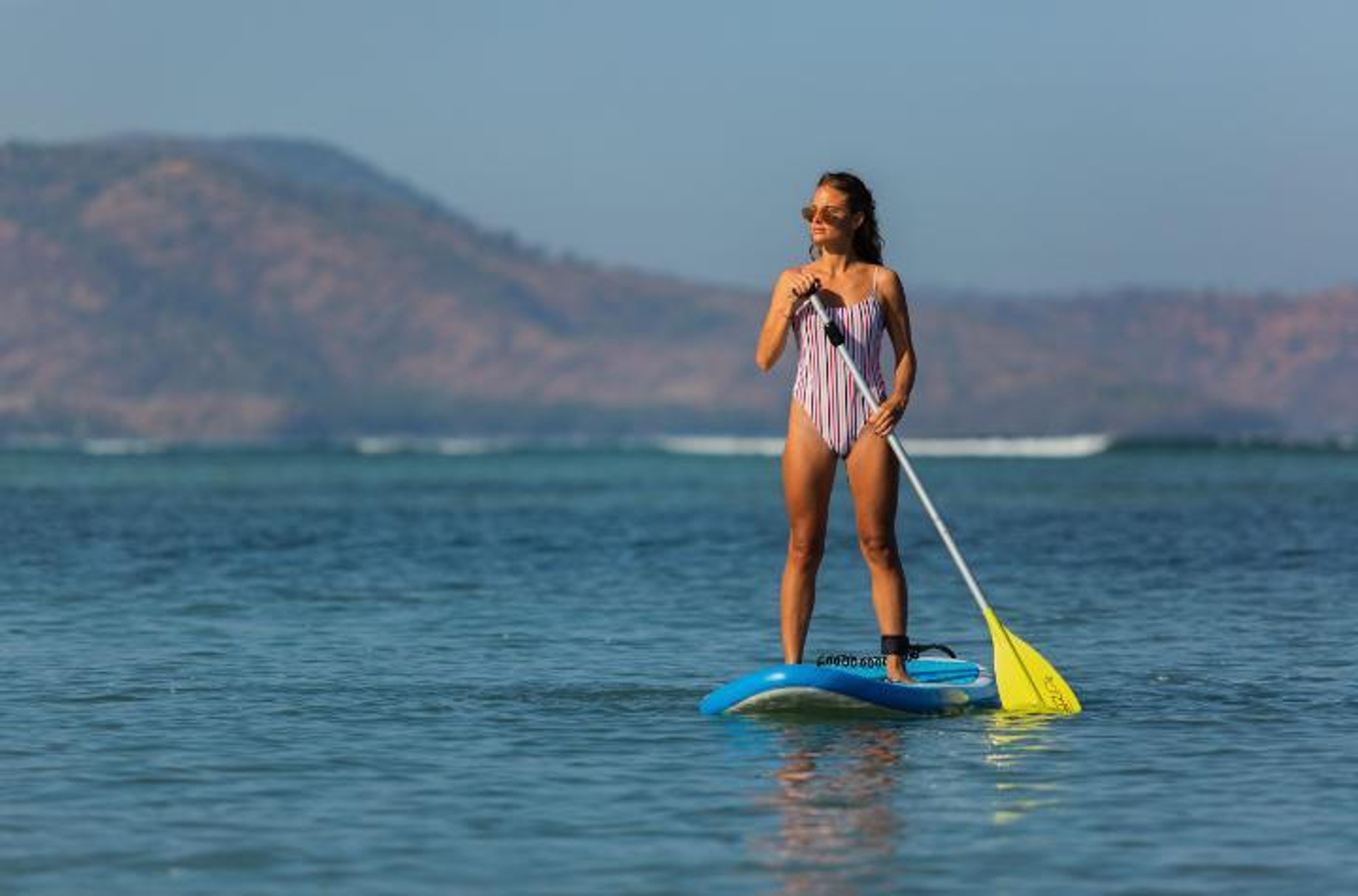 Woman on a blue stand-up paddleboard holding a yellow oar