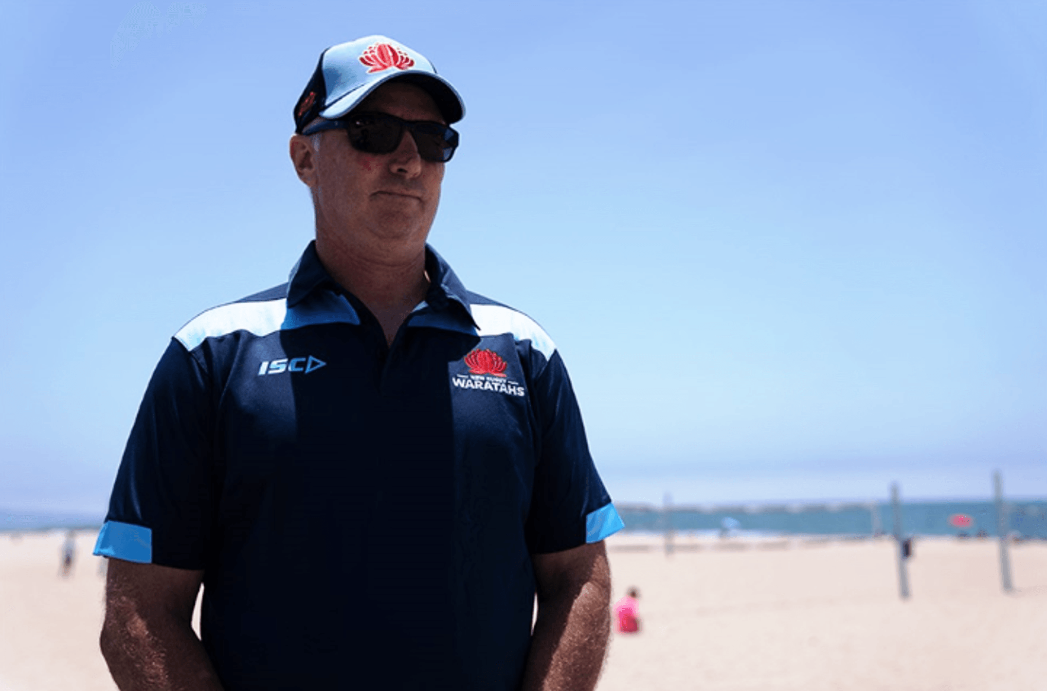 Man wearing NSW Waratahs polo and hat at a beach