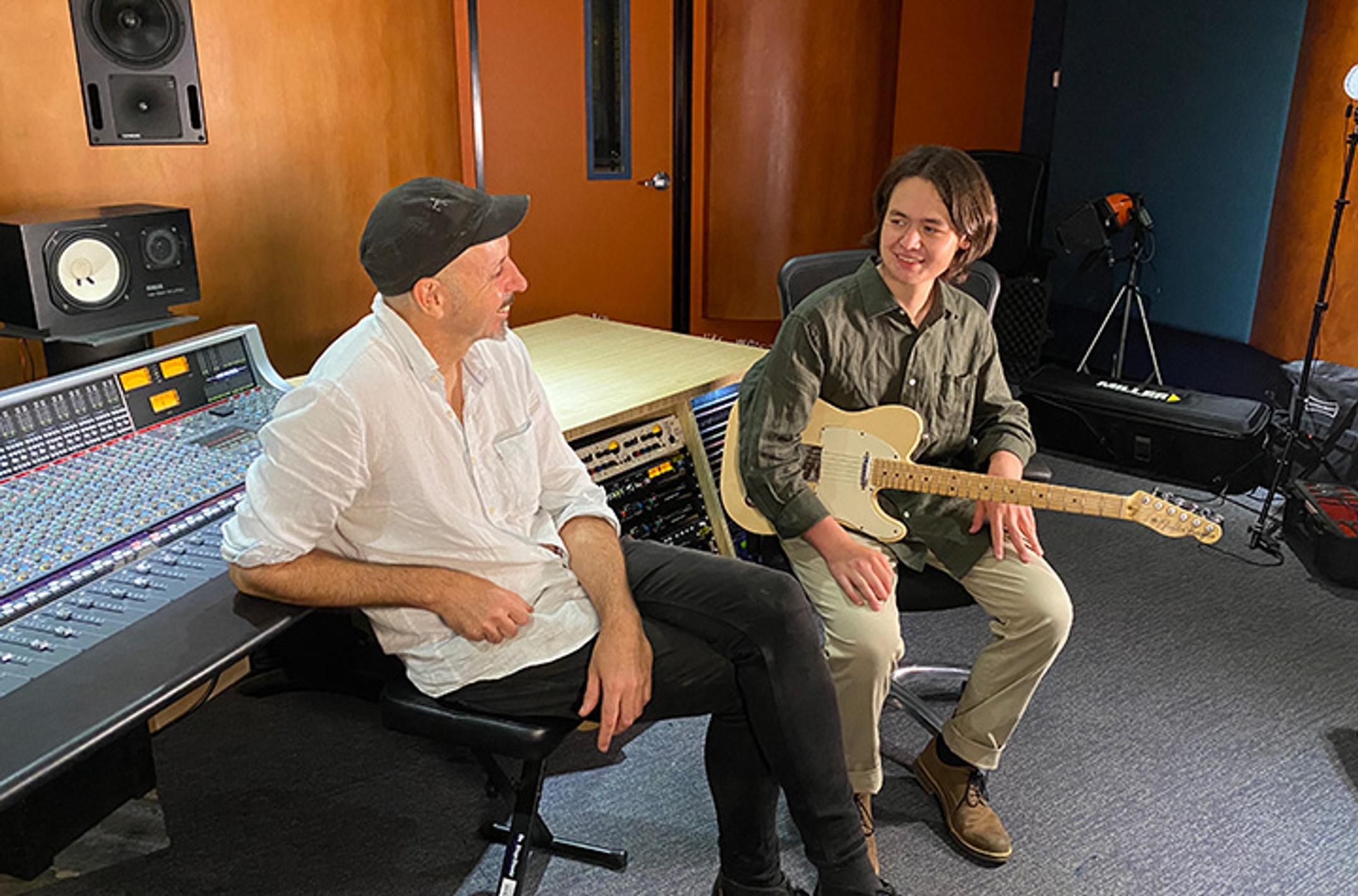 man on left with student holding guitar in music studio