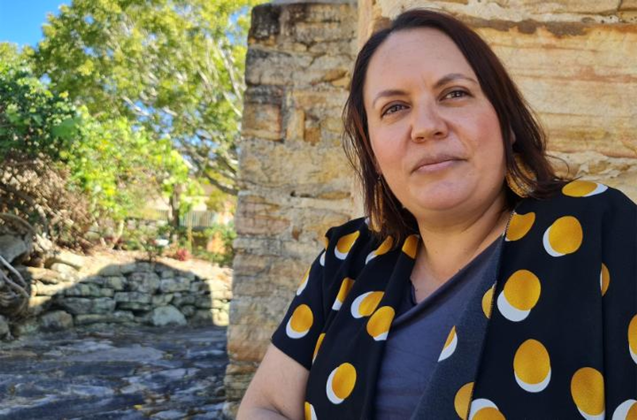 Woman sitting outside beside sandstone wall