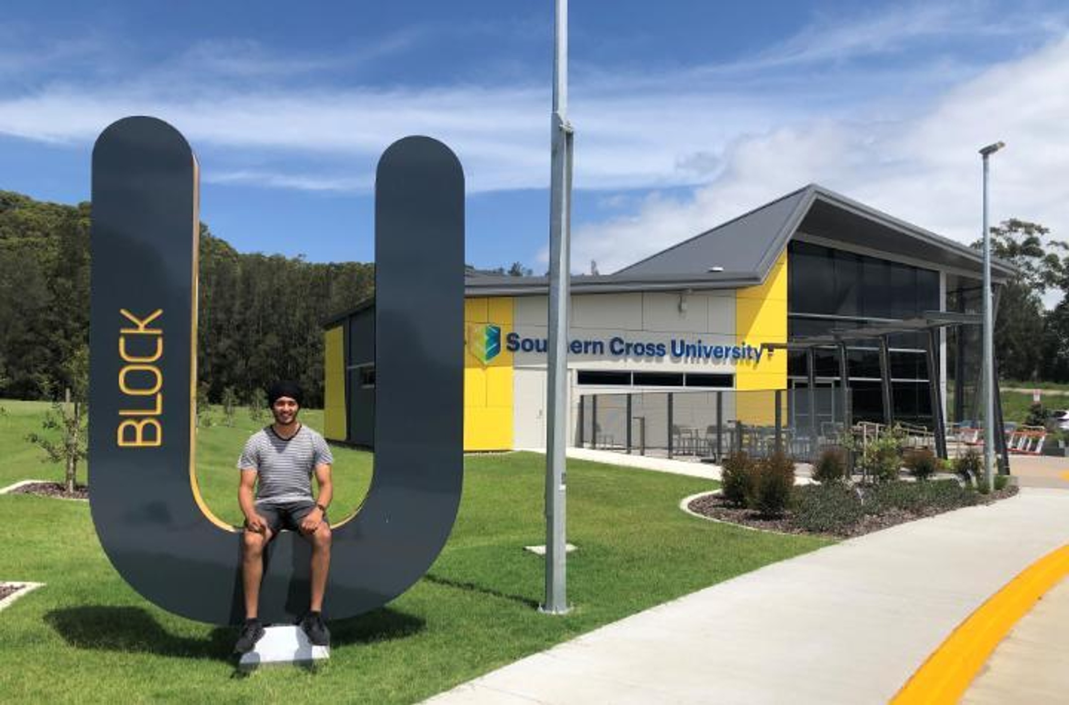 Student sitting on a large U-shaped letter outside a Southern Cross University building