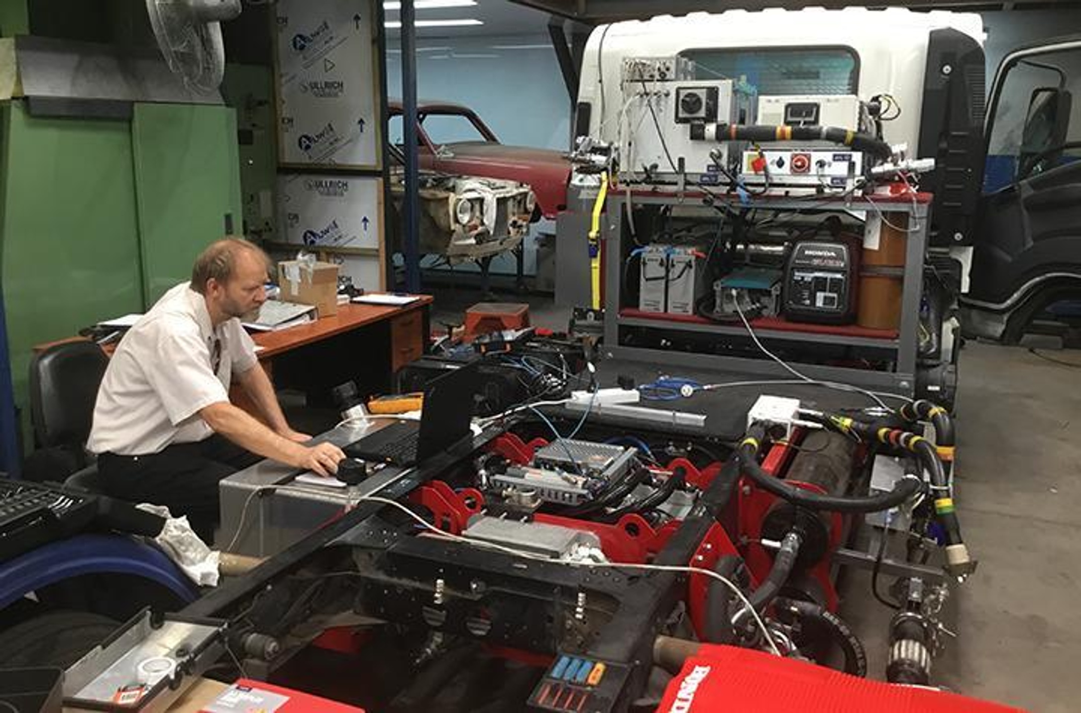 Man in front of a laptop working on the engine of a truck