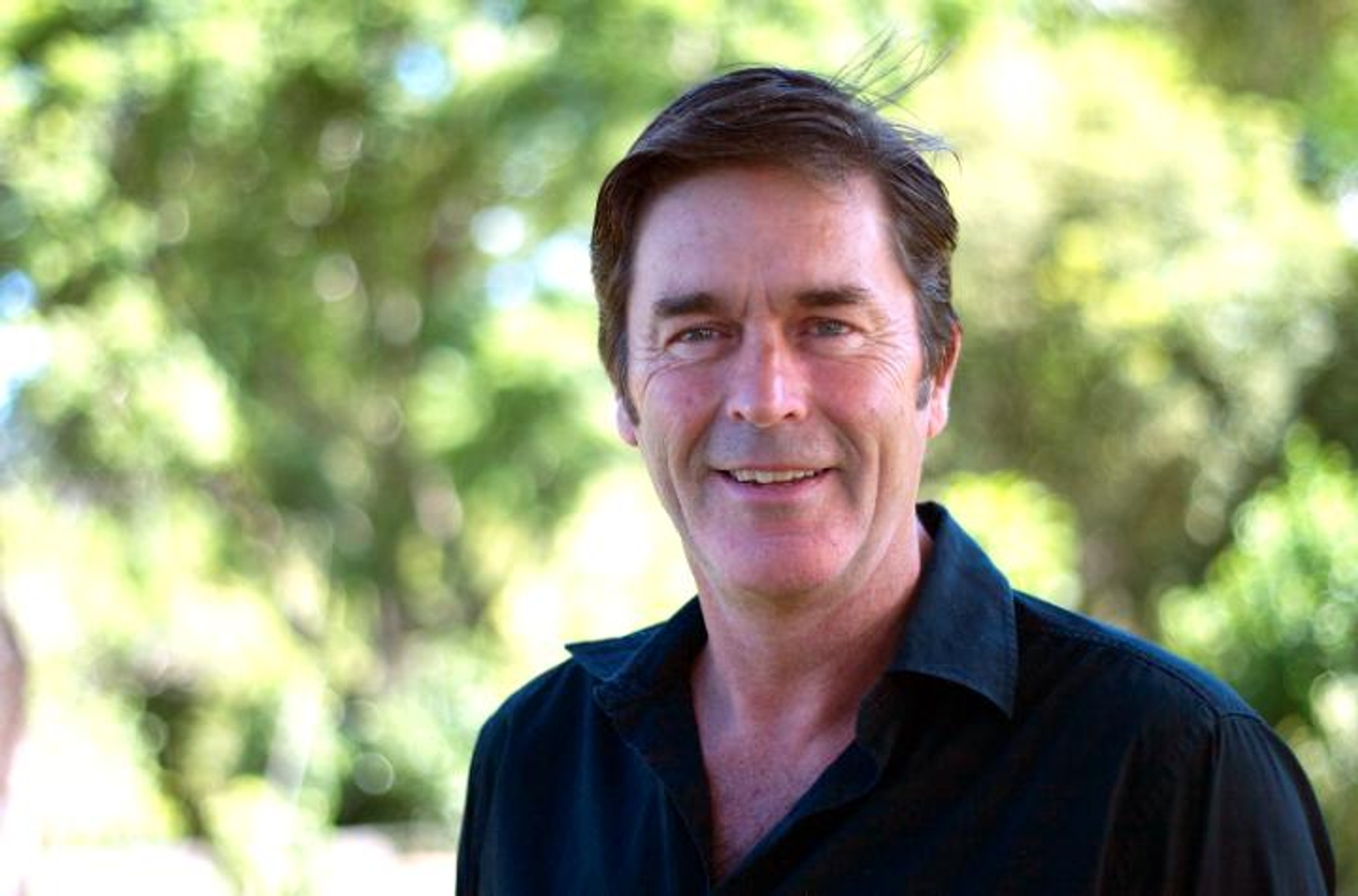 A man smiling and wearing a dark shirt