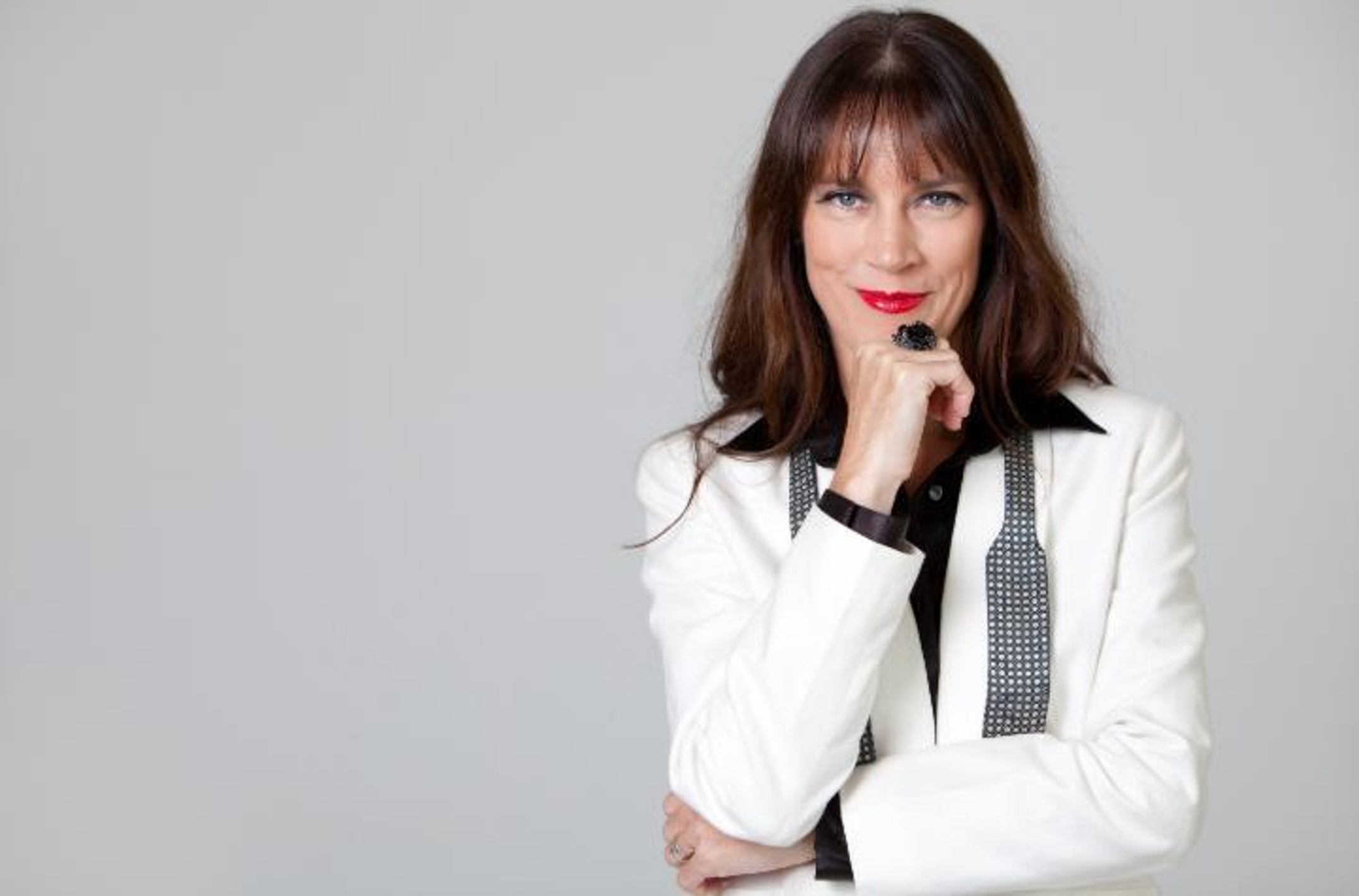 A woman with long dark hair wearing red lipstick and a white suit