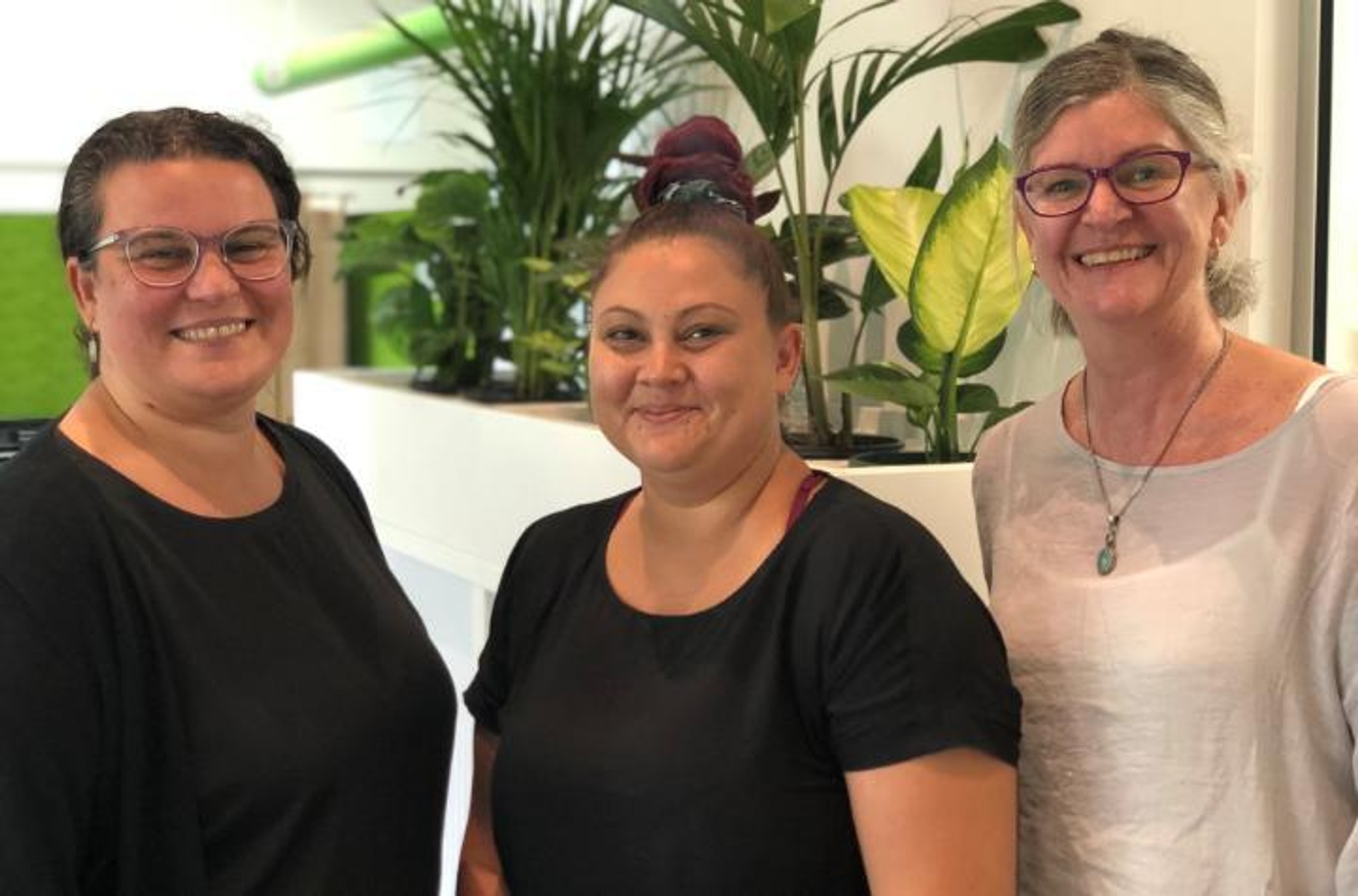 Three women in an office setting in front of pot plants