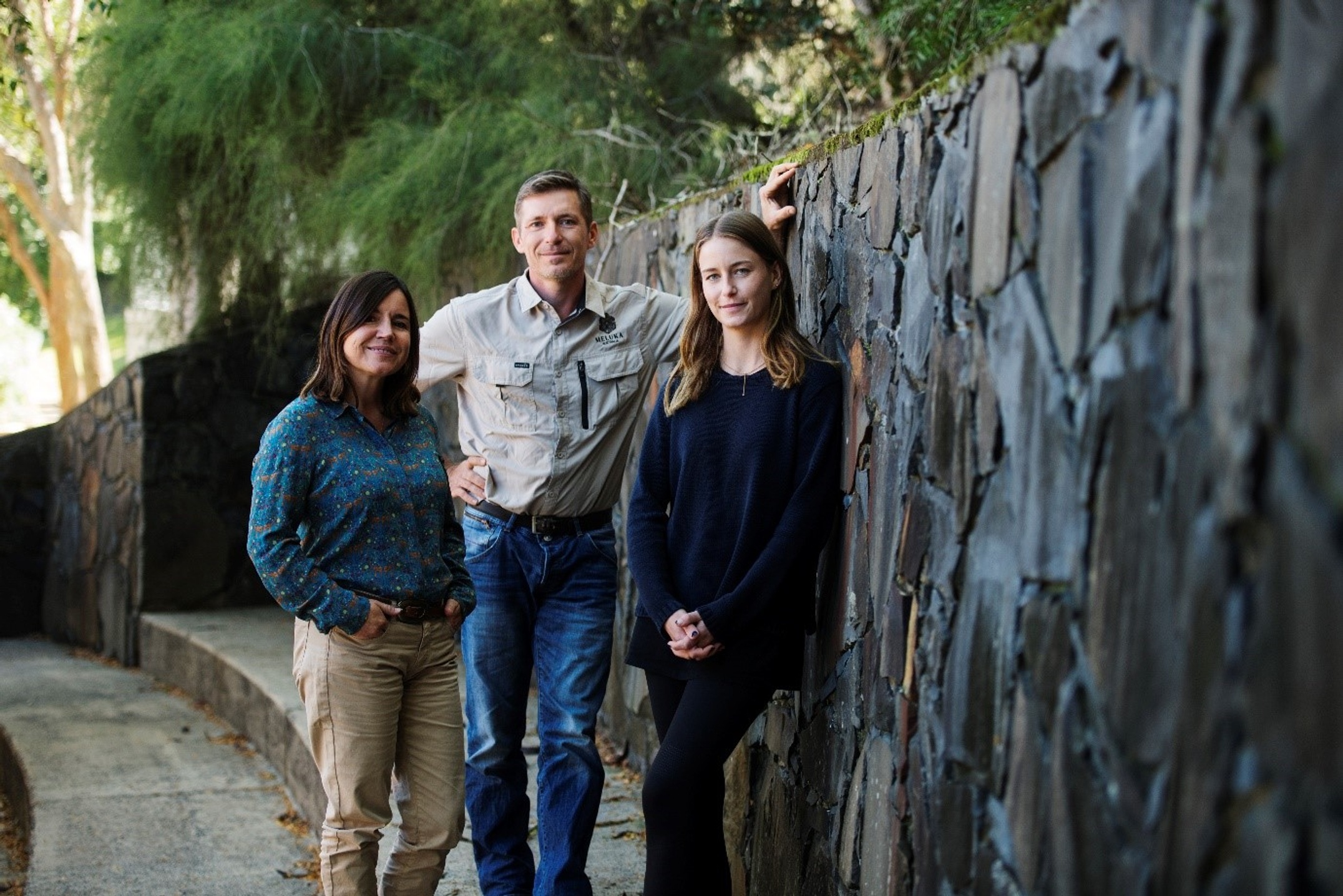 Three people standing next to a stone wall