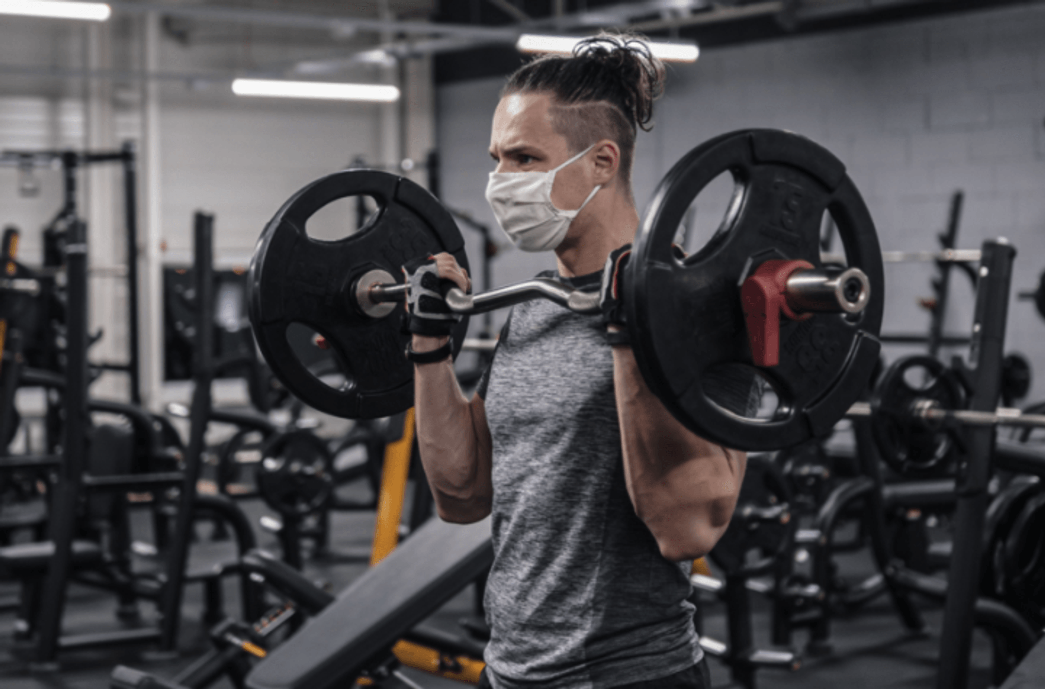 Man wearing a mask lifing weights in a gym