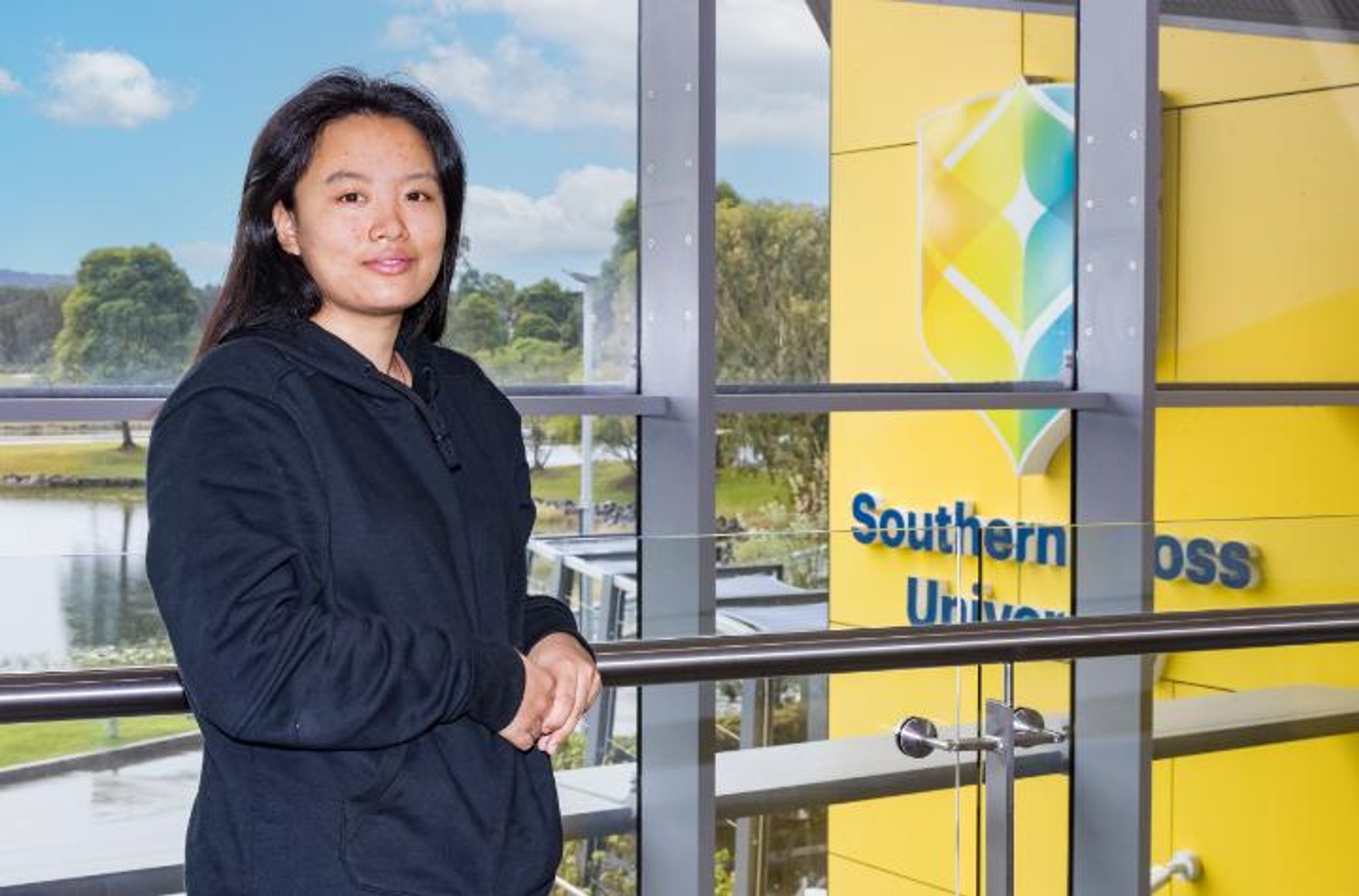 A woman stands in front of a glass edifice with the Southern Cross logo in the background