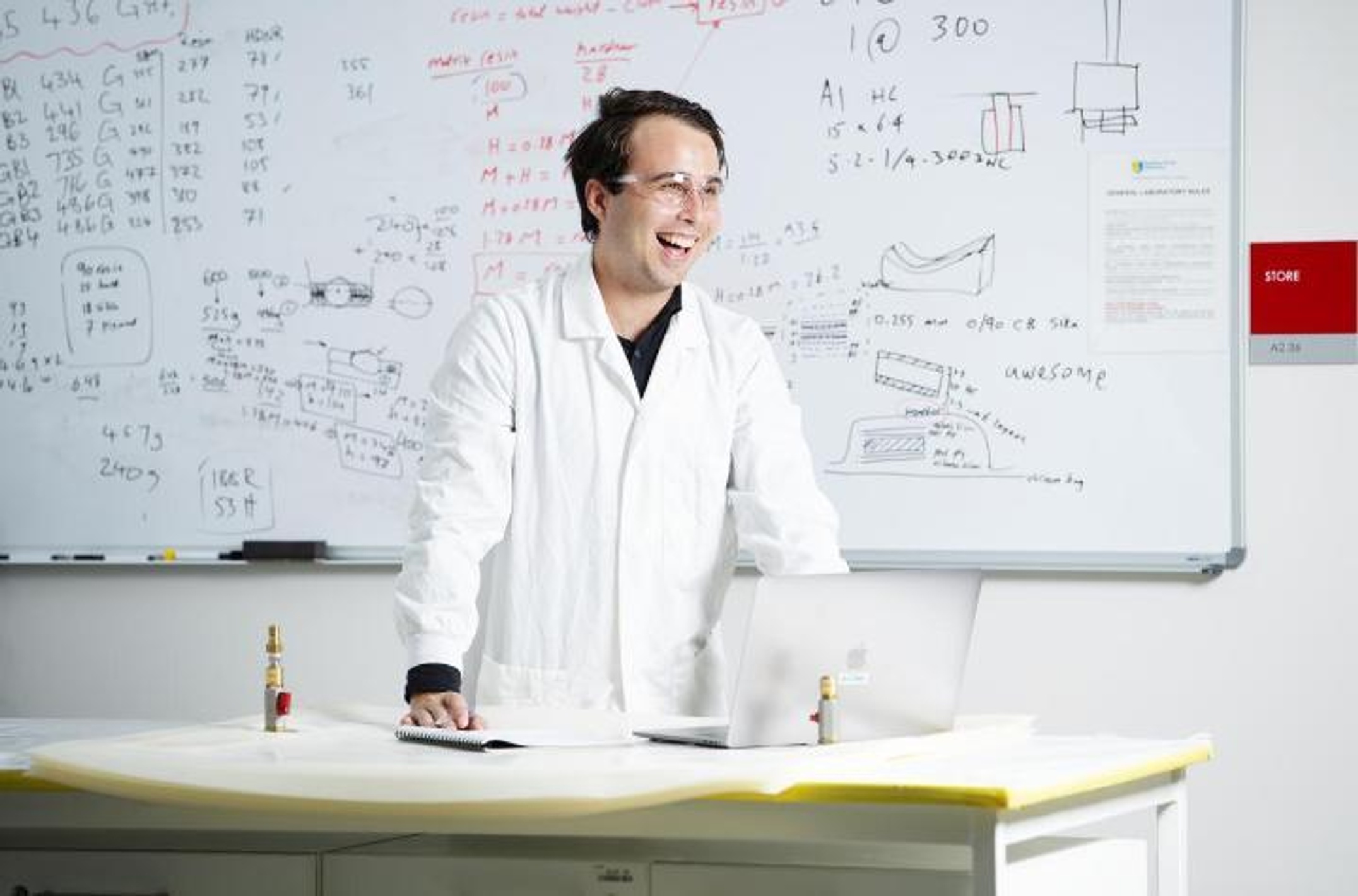 Engineering student in lab coat in front of whiteboard with mathematical calculations