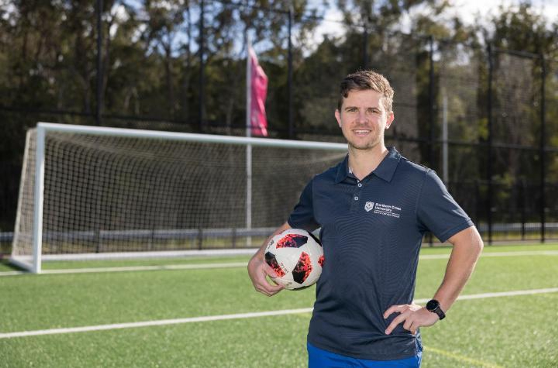 A man with a football stands in from of a soccer net