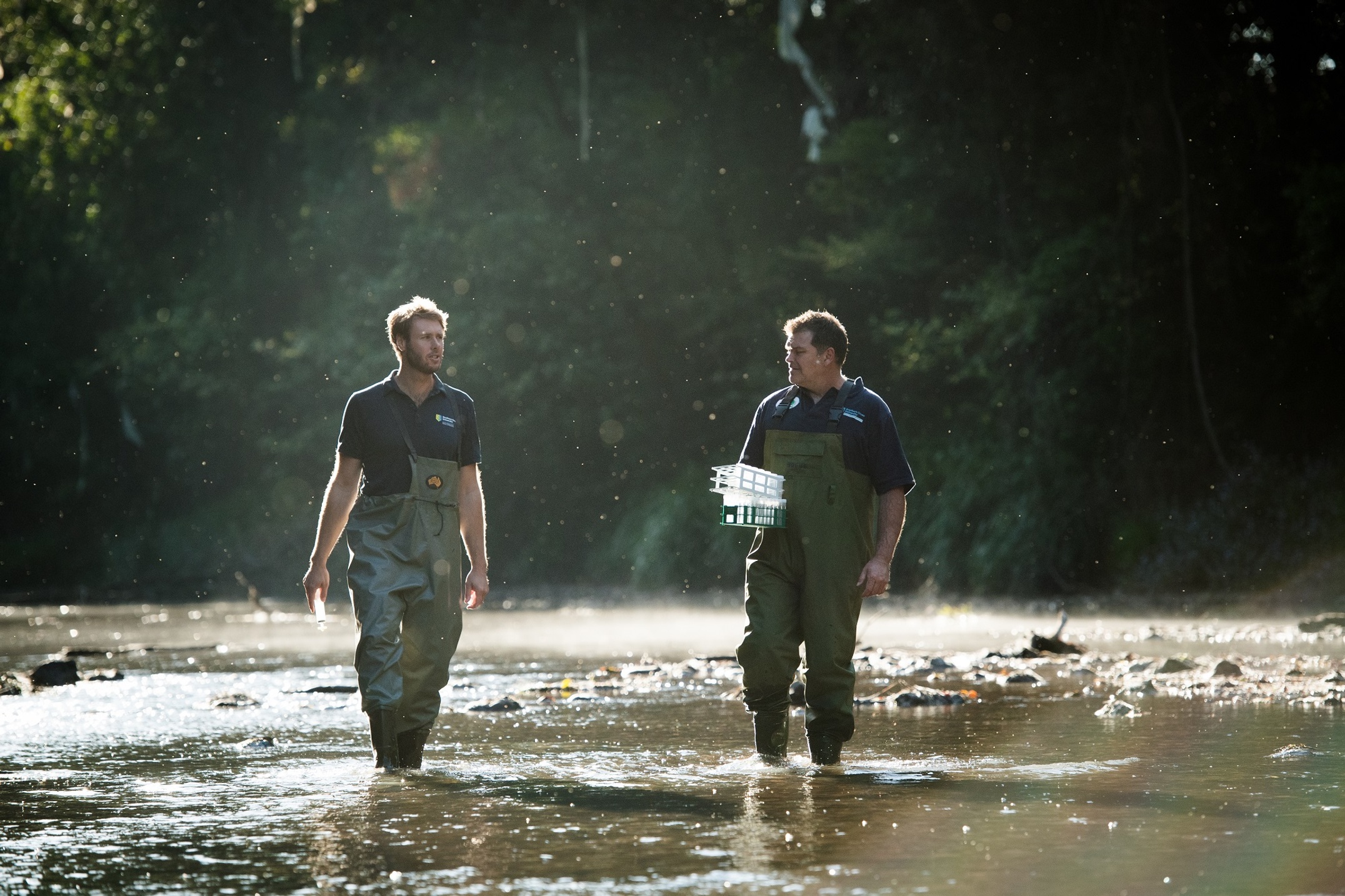 Two men walking in waders in a shallow river bed