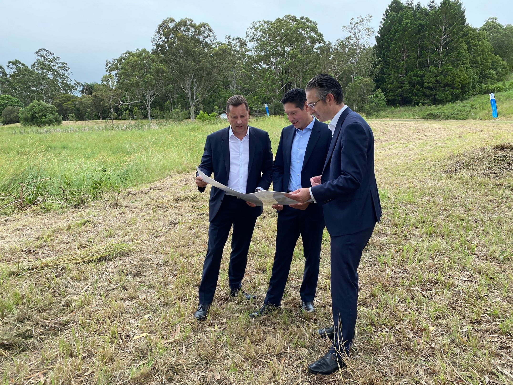Three men examine a map in a green field