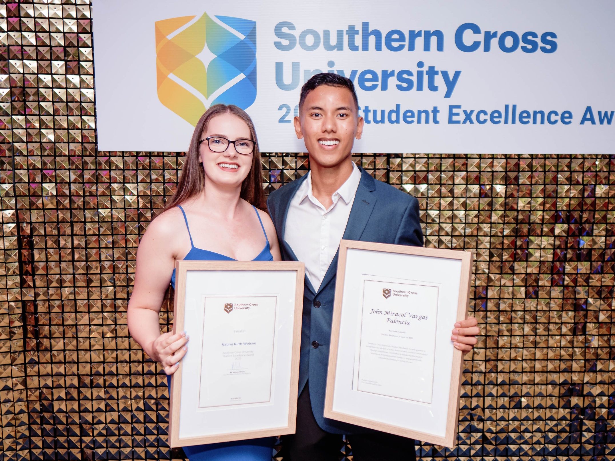 Two students holding framed certificates