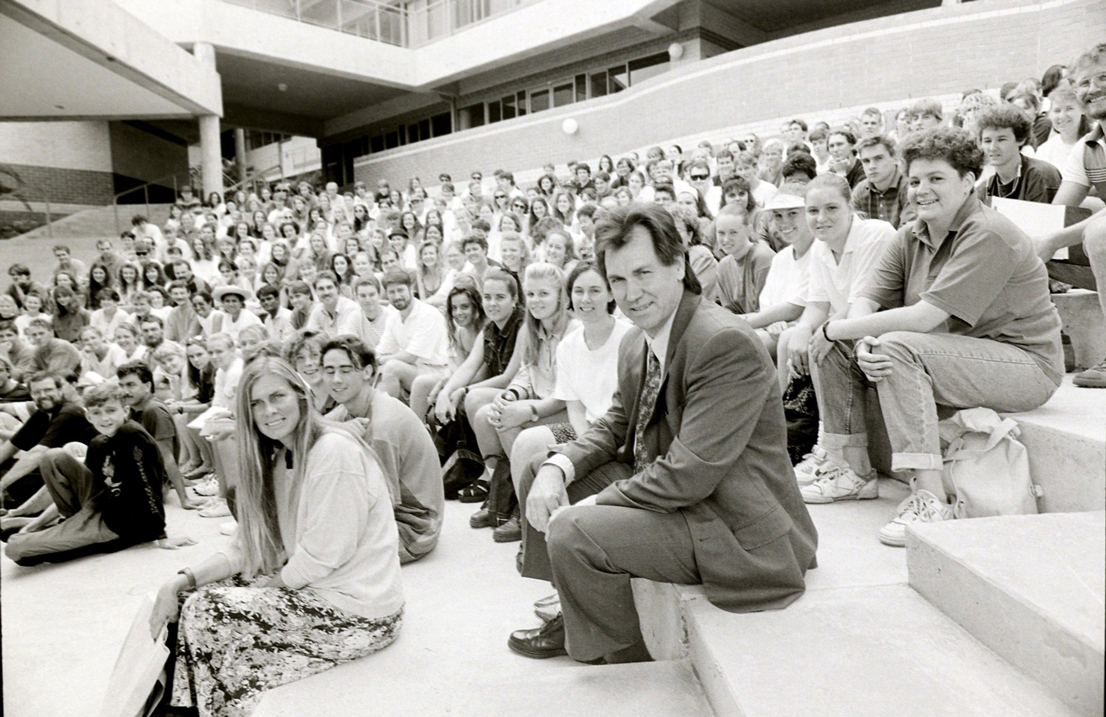 A group of people sit on tiered concrete steps looking at the camera