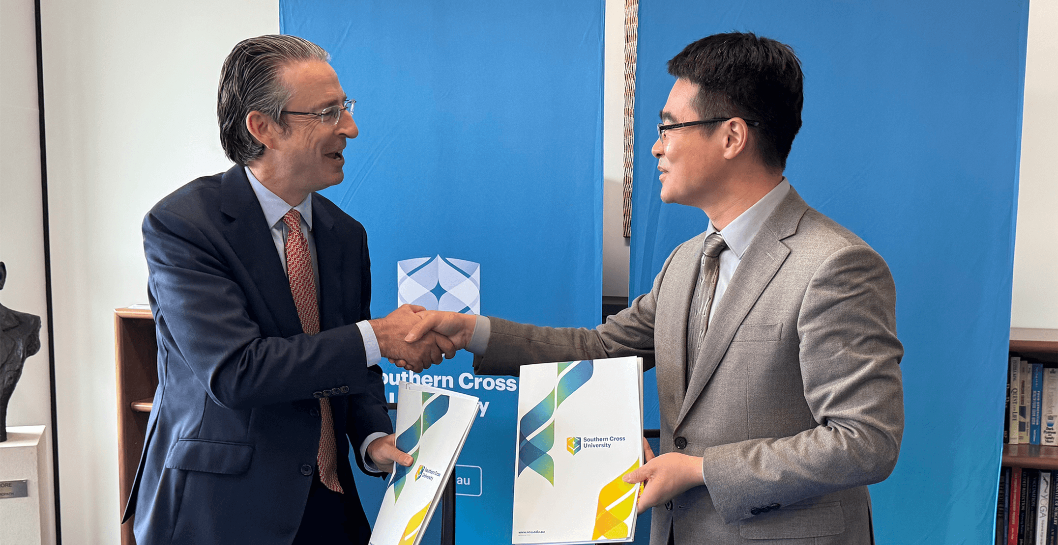 Two Professors in suits holding folders and shaking hands