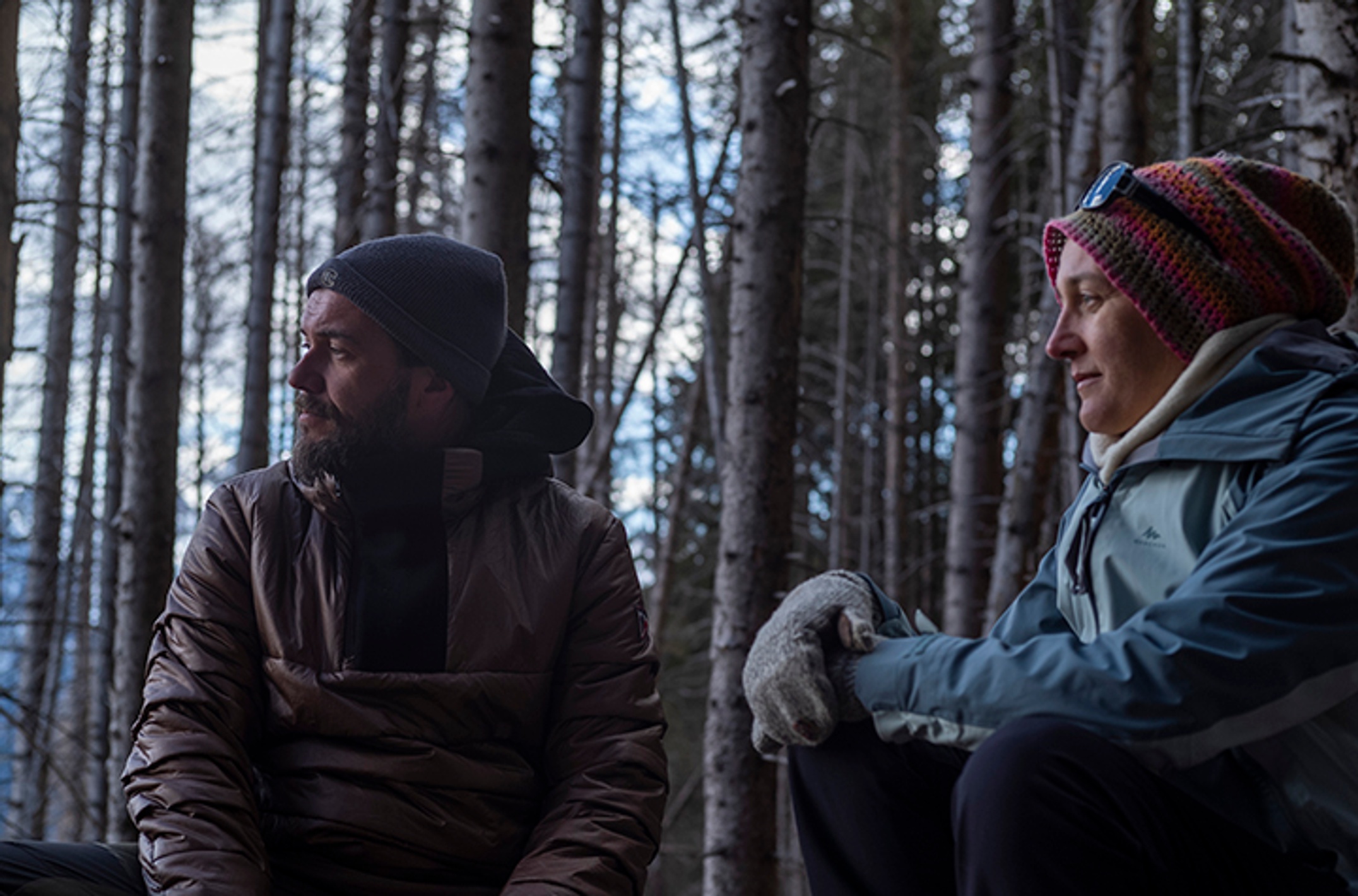 A man and woman wearing warm clothes sitting in a forest