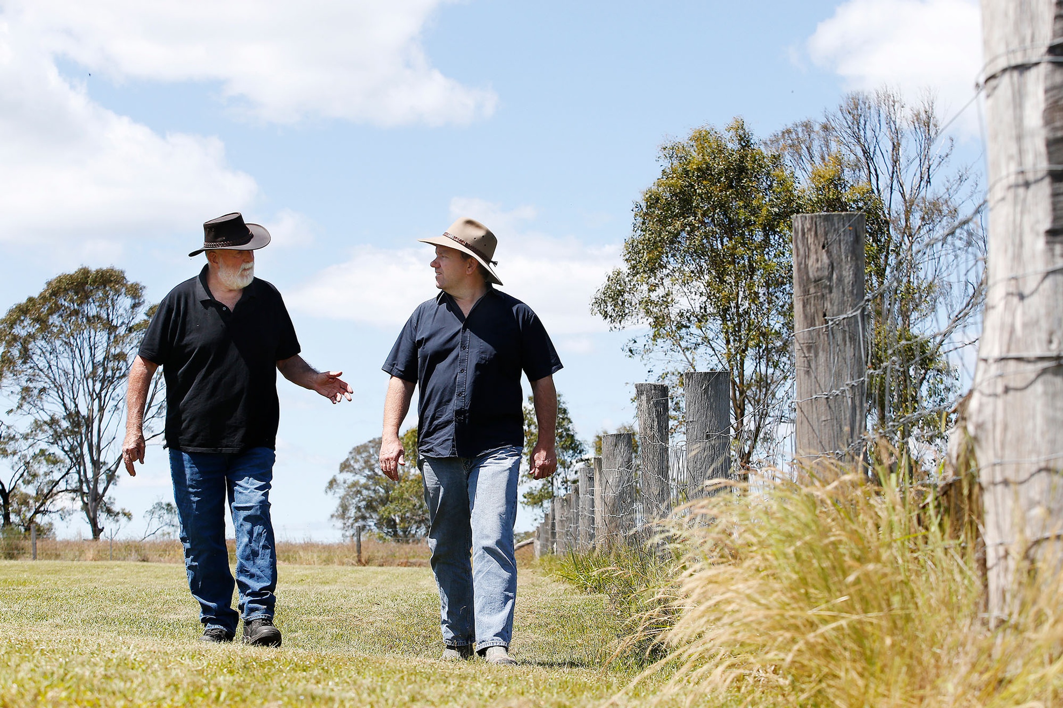 Two farmers walking and talking next to fence