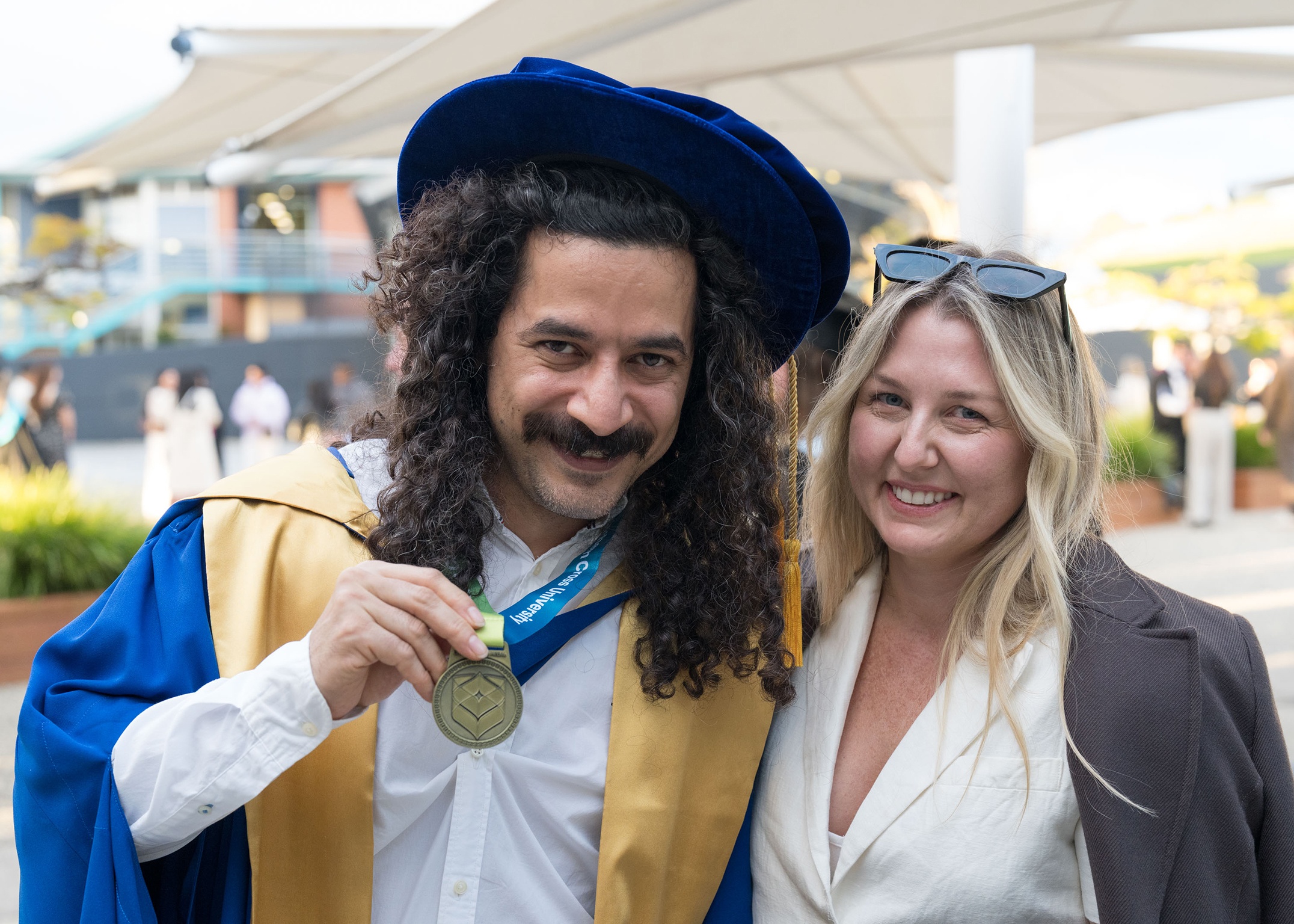 Graduate with rob and gown holding medal and smiling with female next to him