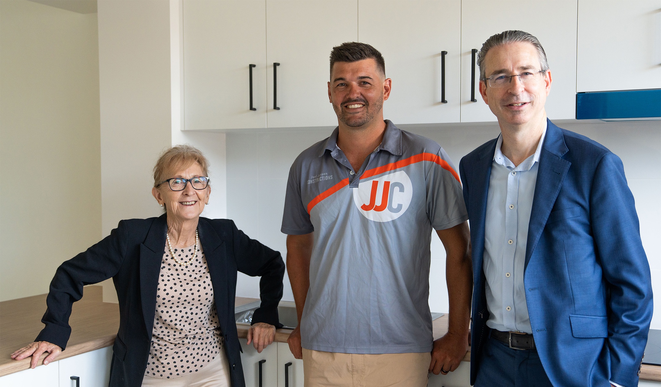 A woman and two men standing in kitchen with white cupboards behind them