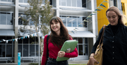 Students walking through Gold Coast campus grounds holding laptop