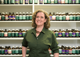 Naturopath Carla O'Brien stands in front of a wall of natural medicines