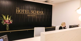Woman sitting at reception desk with The Hotel School Brisbane sign in background