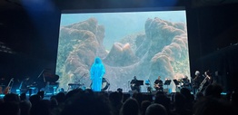A band on stage against a backdrop of coral projected on the screen.