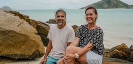 A man and woman sitting on rocks with the ocean and an island in the background