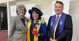 Women in academic dress with medal standing between woman and man