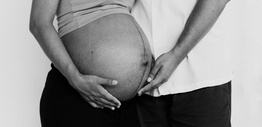 A black and white image of the belly of a pregnant women with male partner touching her belly