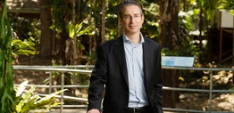 A man in a business suit and open shirt standing outside in a garden.