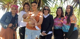 A group of women in front of a pandanus tree, with one of them holding a baby