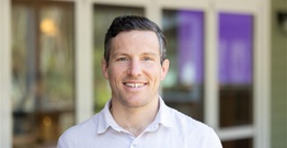 Headshot of man in button up shirt smiling at camera