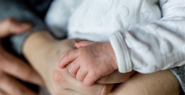 Newborn baby's hand resting on adult hand