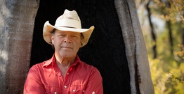 Man in cowboy hat standing in front of large tree trunk