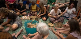 A group of Indigenous and non-Indigenous women sitting on the floor making string from plant fibres.