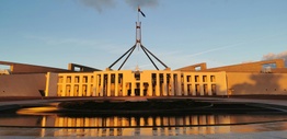 A modern building with a flagpole reflecting in pond below.