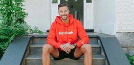 A man with a beard sitting on a set of stairs wearing a red hoodie