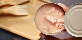 An open can of tinned tuna next to a wooden cutting board